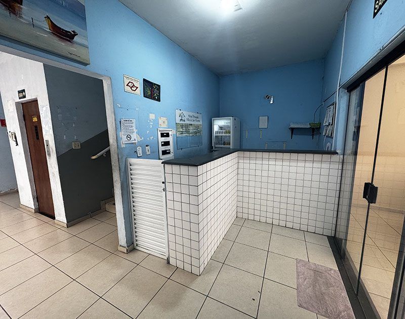 Área de recepção com balcão revestido de azulejos, paredes azul-claras, piso de azulejo, uma porta à esquerda e uma porta de vidro à direita.