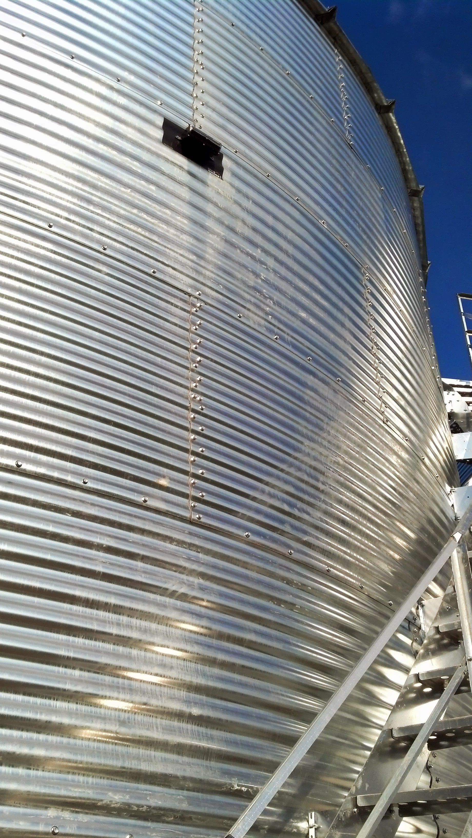 Close-up of a large silver corrugated metal silo against a blue sky