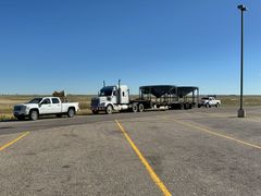 Pickup trucks and a semi hauling a flatbed trailer in an empty parking lot under a clear blue sky