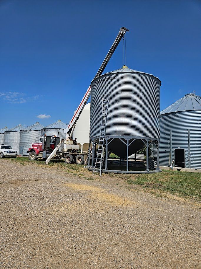 Grain silos with a raised auger loader on a gravel farmyard under a clear blue sky