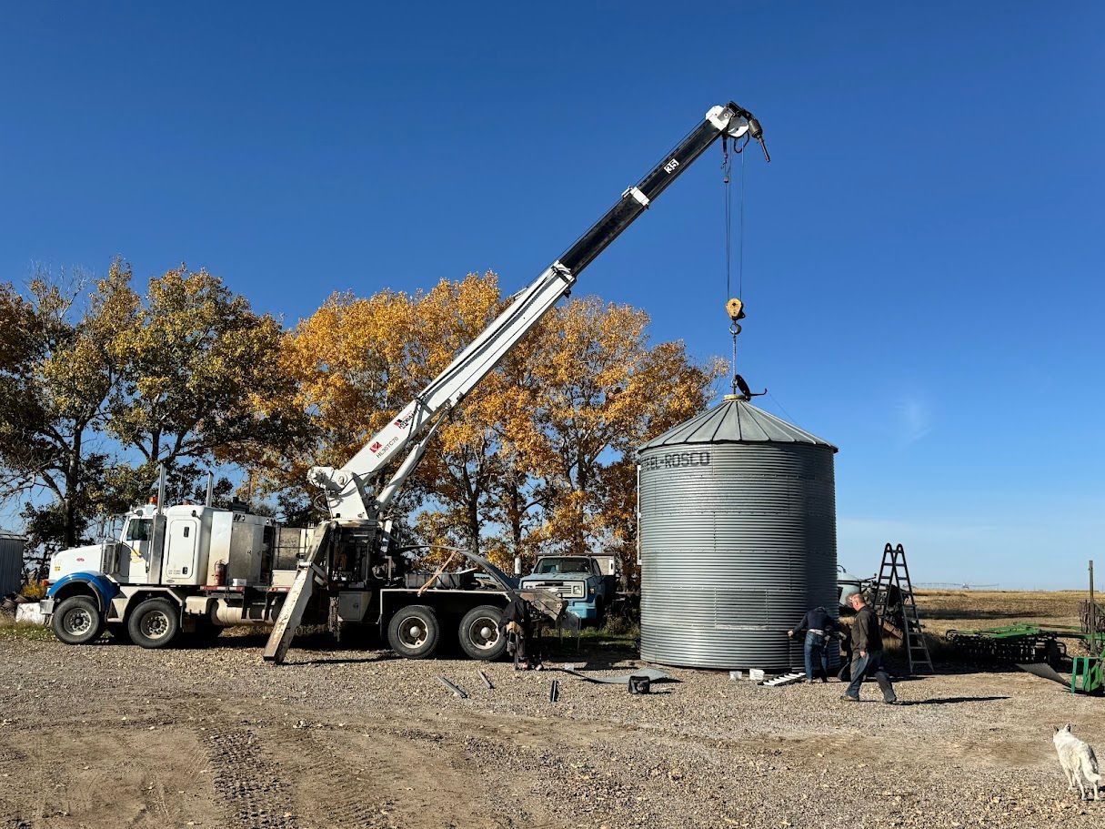 Crane lowering a large metal tank at a construction site under a clear blue sky