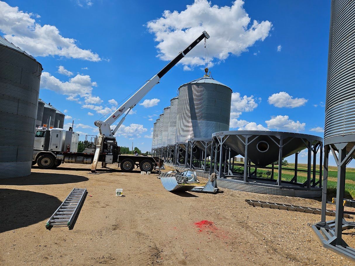 Construction site with crane lifting equipment near large cylindrical tanks under a bright blue sky