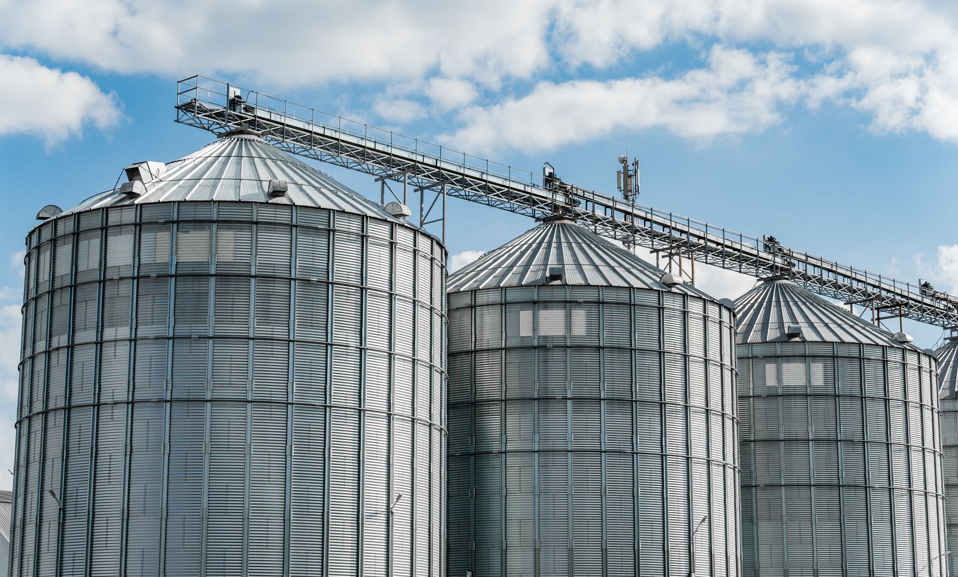 Grain silos with conveyor belt, blue sky with clouds.