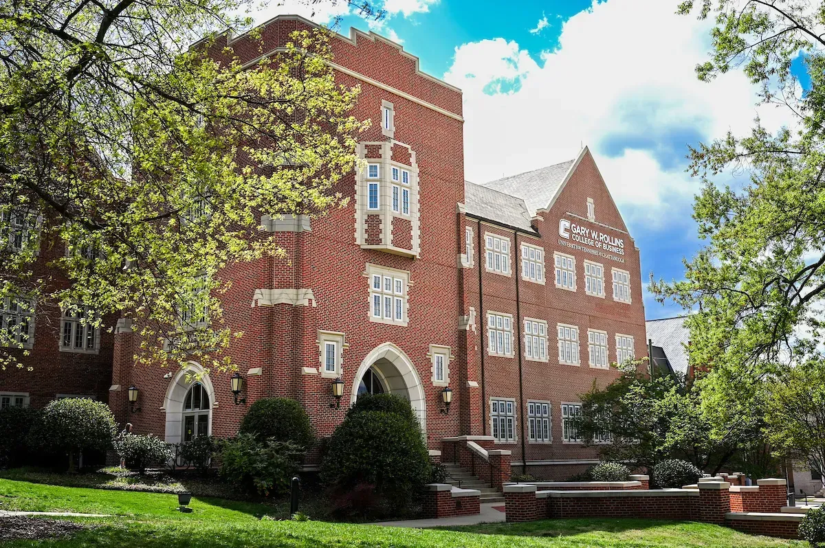 A large brick building with a lot of windows is surrounded by trees and grass.