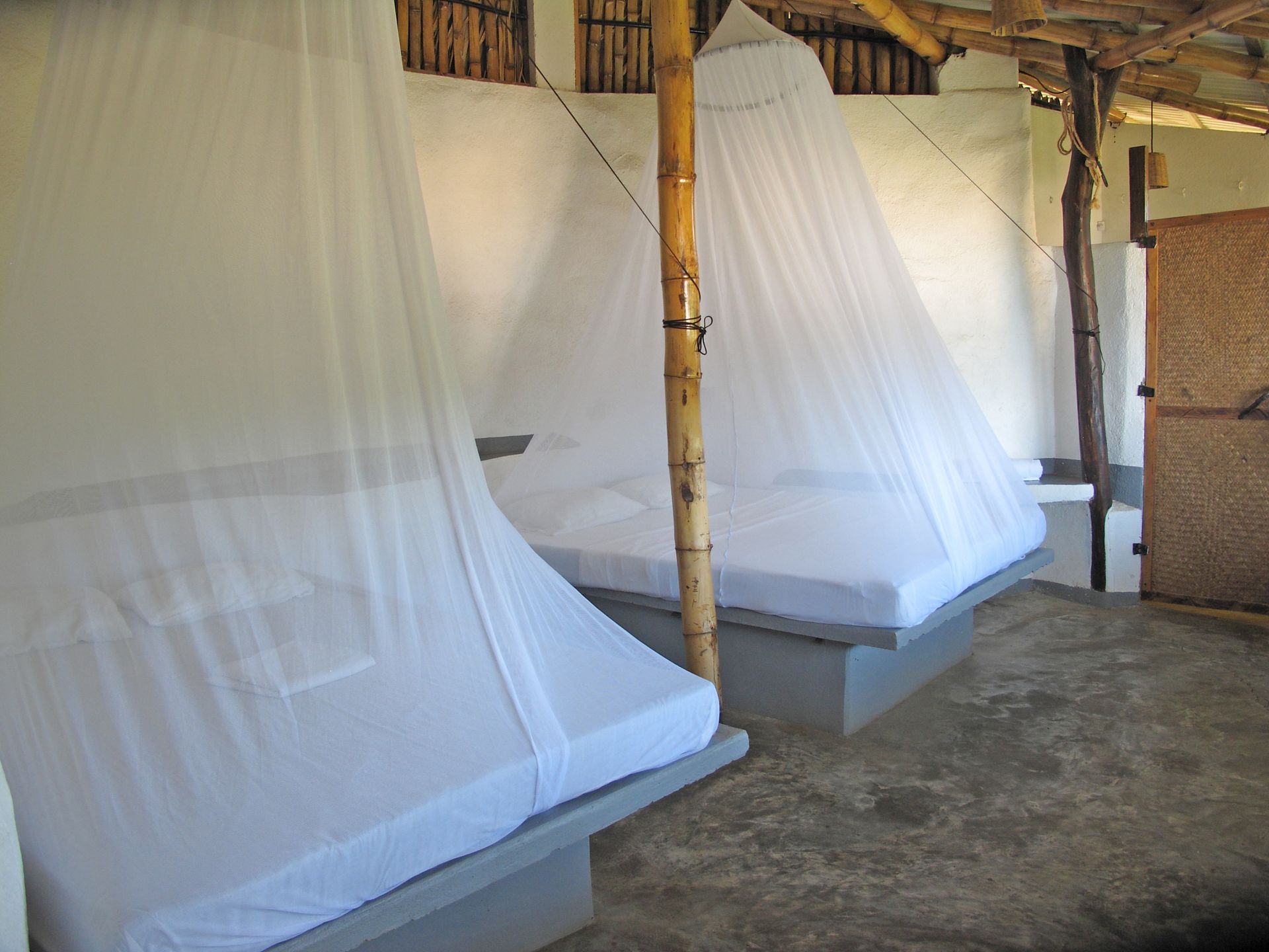 Dos camas con mosquiteras en una habitación sencilla en posada del arquitecto