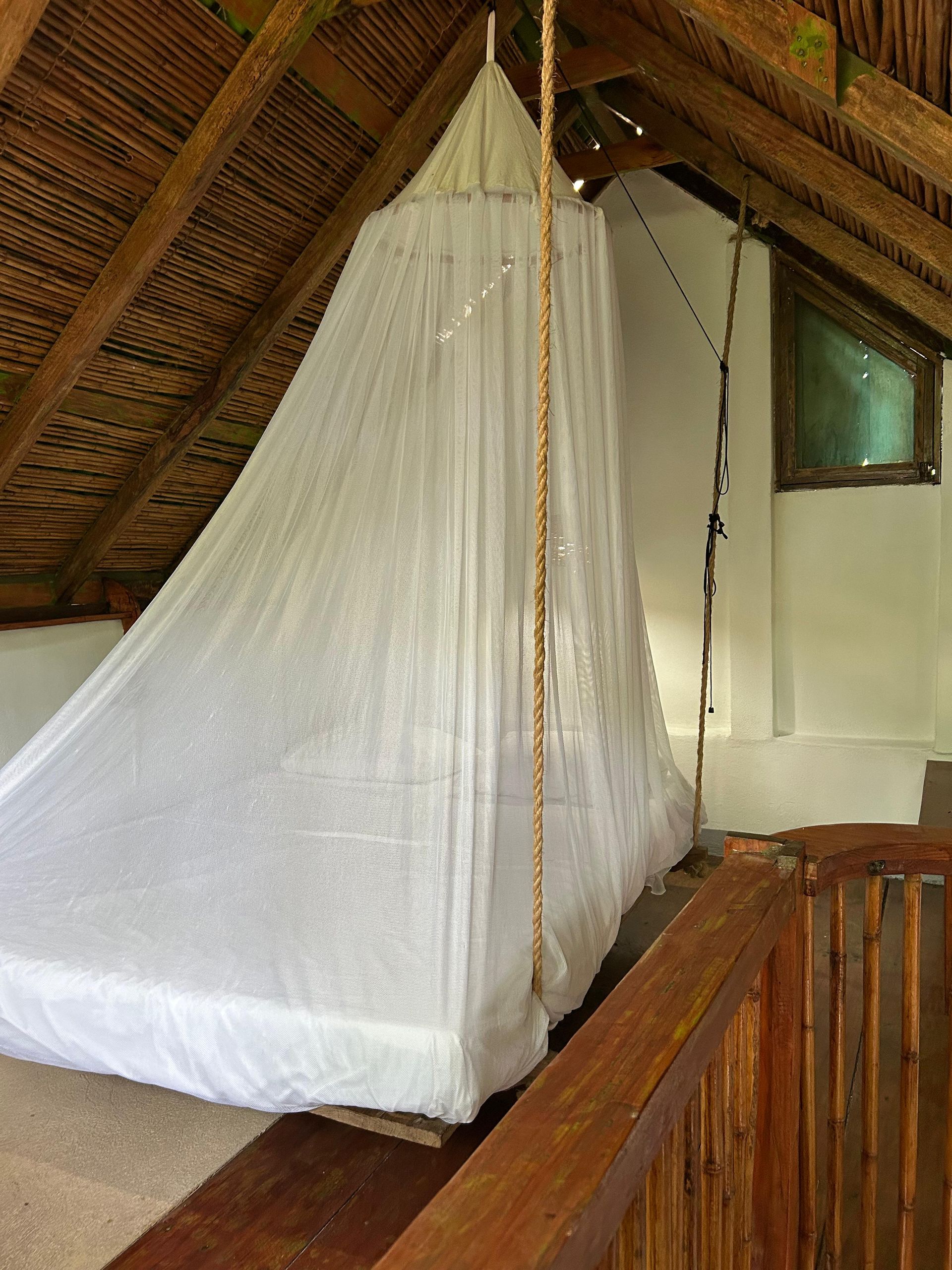 Mosquitera blanca extendida sobre una cama en una habitación con techo de paja en posada del arquitecto en mazunte, oaxaca