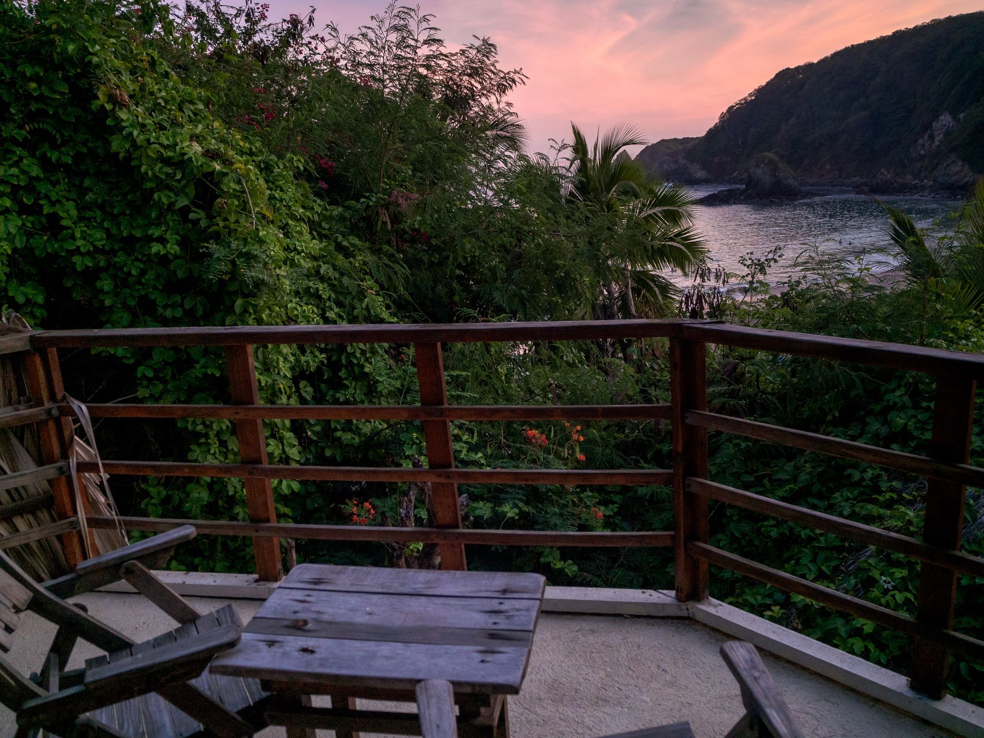 Terraza de madera con sillas y mesa con vistas a la bahía al atardecer en mazunte, oaxaca