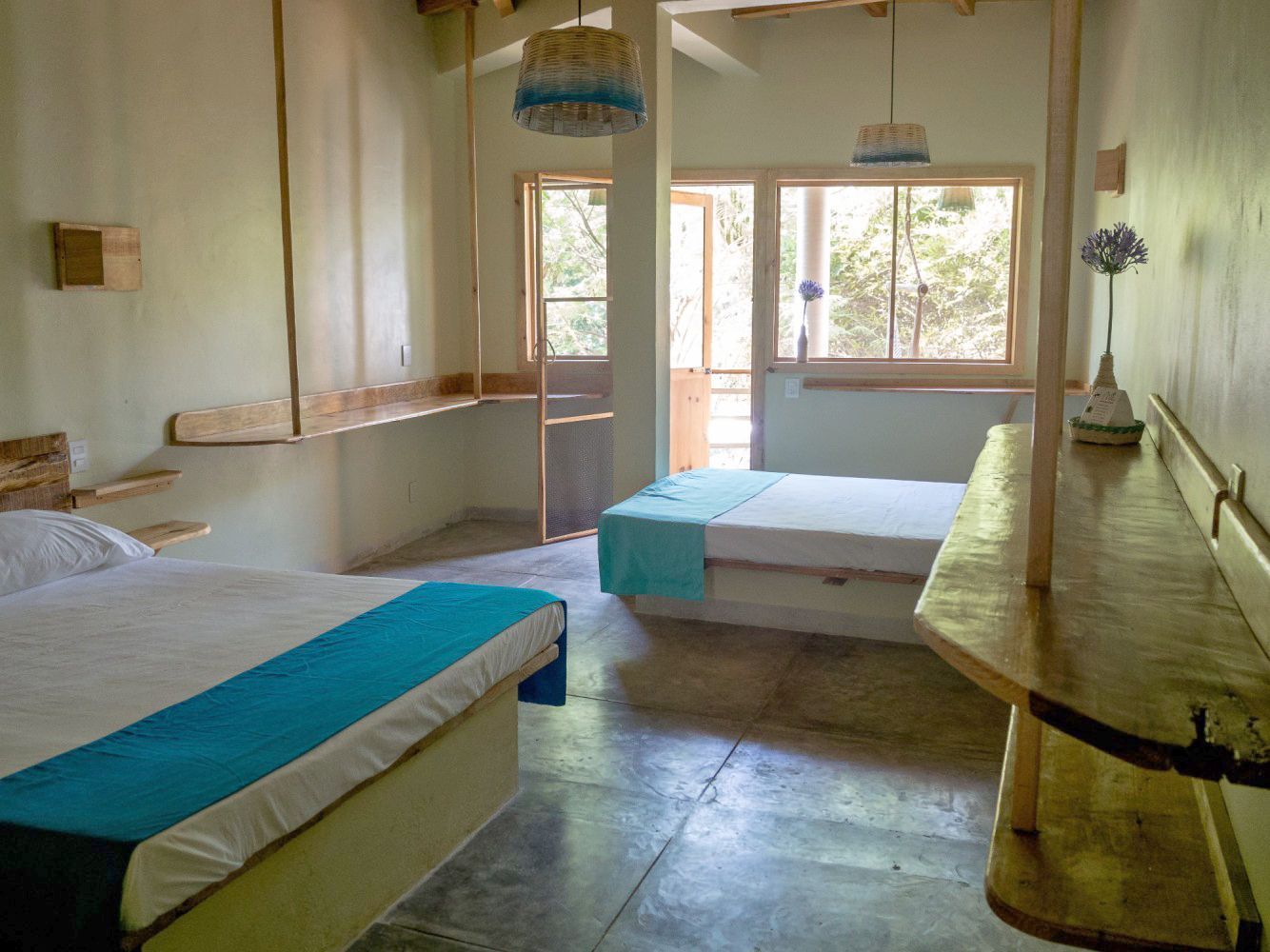 Dormitorio con dos camas, mobiliario sencillo de madera, balcón y luz natural en posada del arquitecto en mazunte, oaxaca