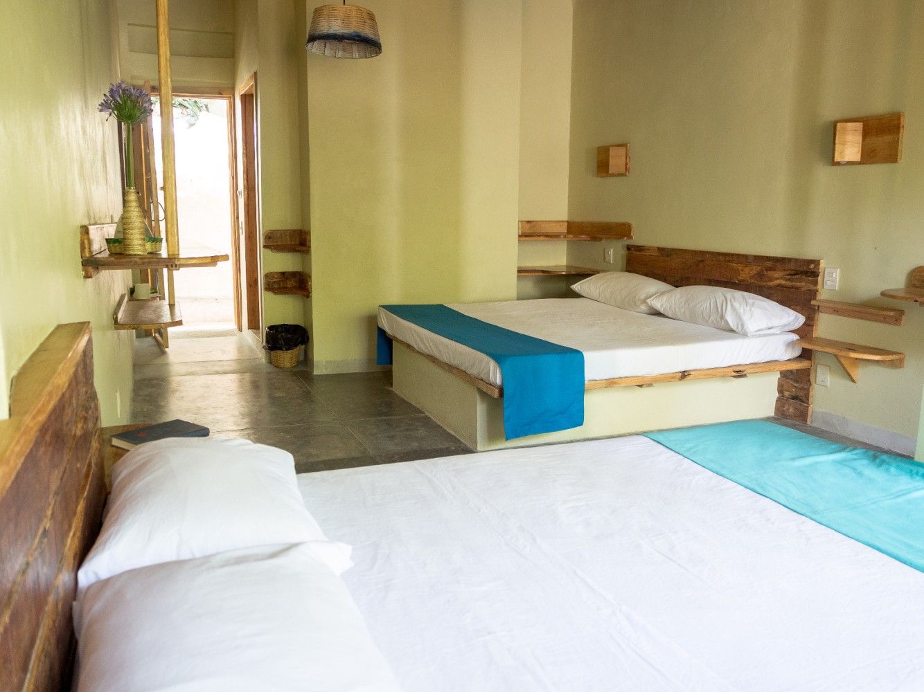 Dormitorio con dos camas, paredes de color verde claro, cabeceros de madera y una puerta que da al exterior.
