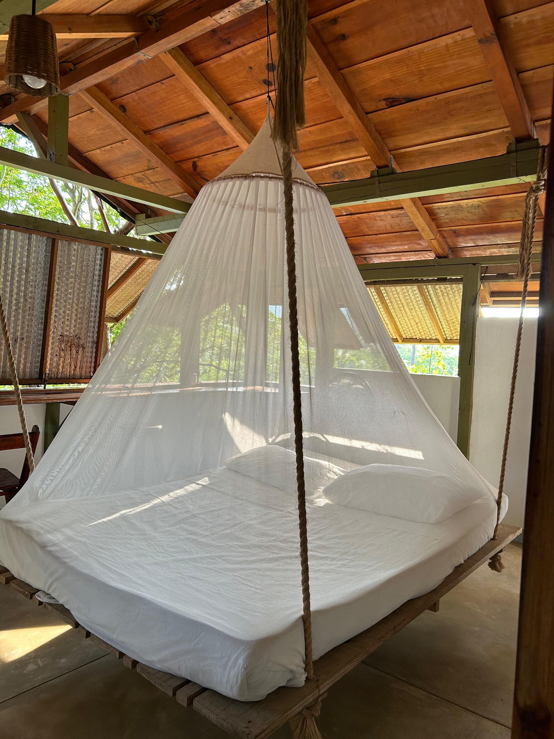 Cama con mosquitera blanca colgando de un techo de madera y bambú en posada del arquitecto en mazunte, oaxaca
