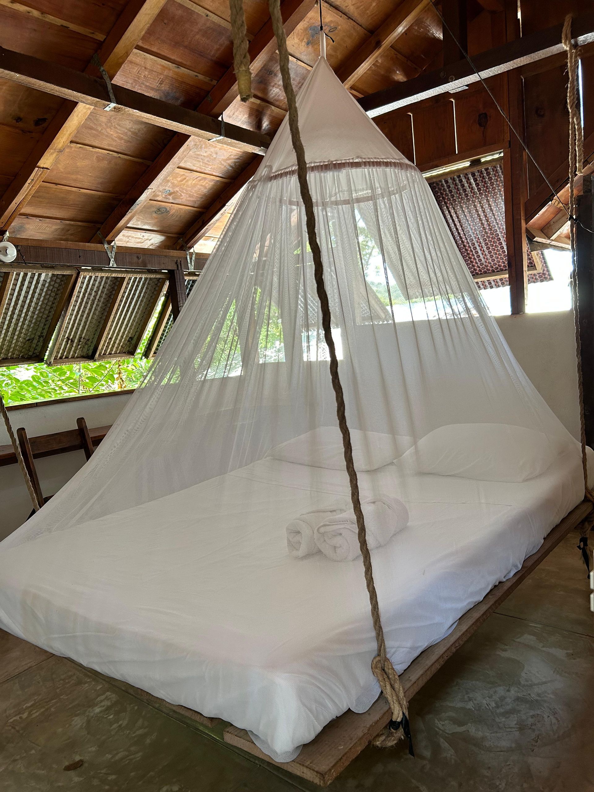 Cama con sábanas blancas y mosquitera bajo techo de madera en posada del arquitecto en mazunte, oaxaca