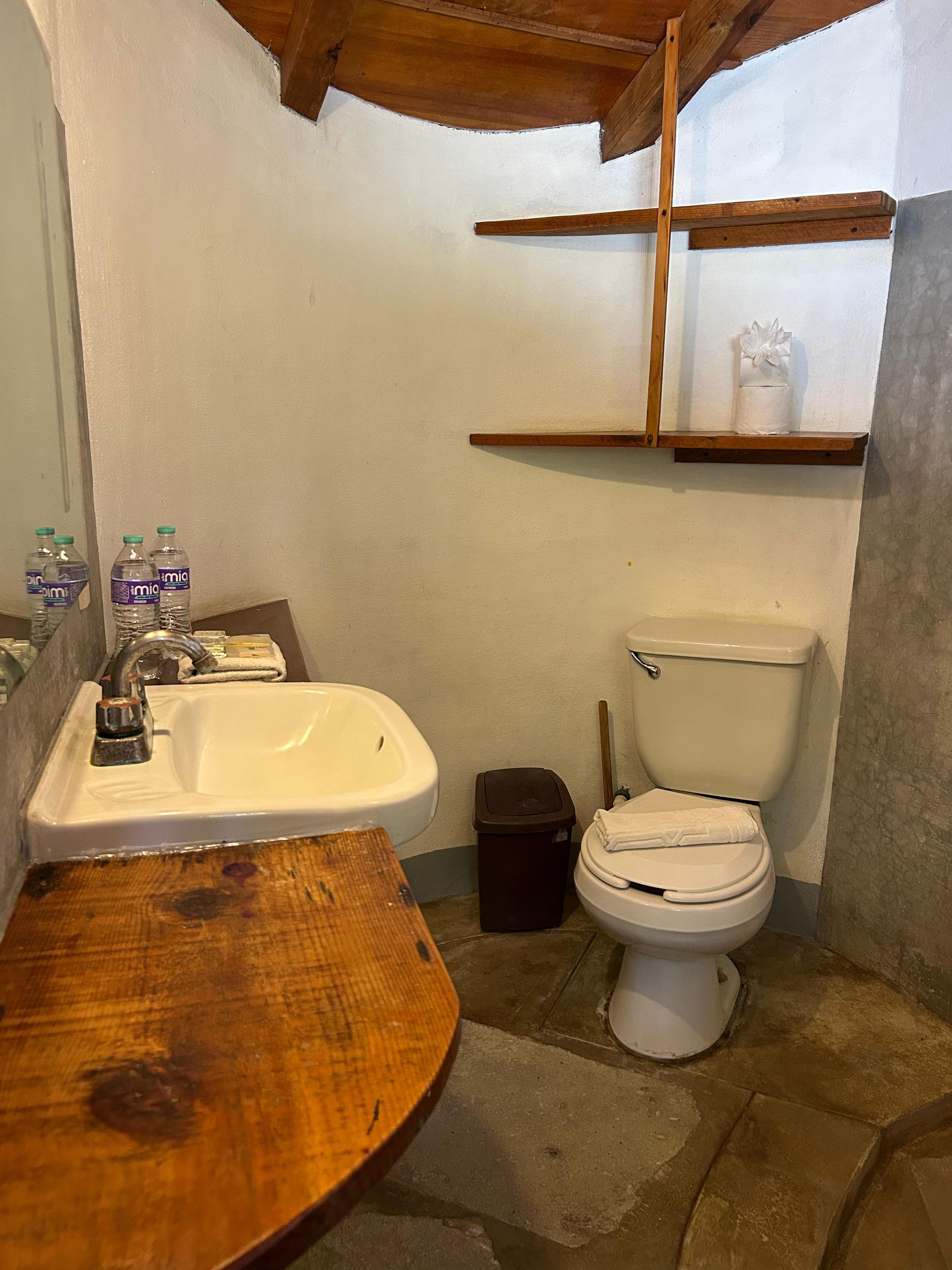Pequeño baño rústico con lavabo, inodoro y estantes de madera en posada del arquitecto en mazunte, oaxaca