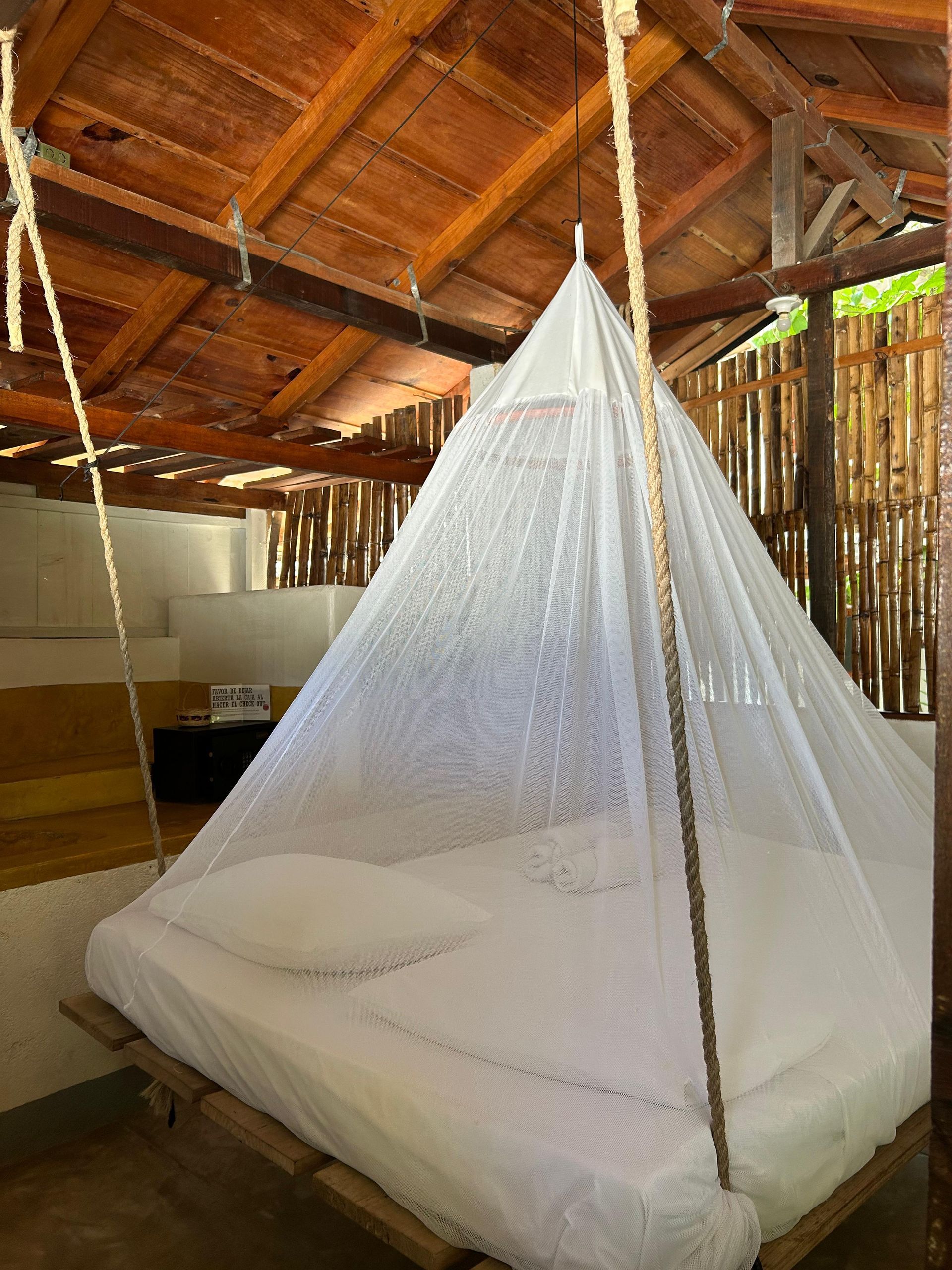 Cama con mosquitera colgando de un techo de madera en un entorno exterior en posada del arquitecto en mazunte, oaxaca
