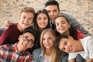 A group of young adults are standing together in front of a brick wall.