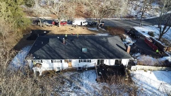 Aerial view of a white house with a dark roof, set in a snowy landscape with a road and bare trees.
