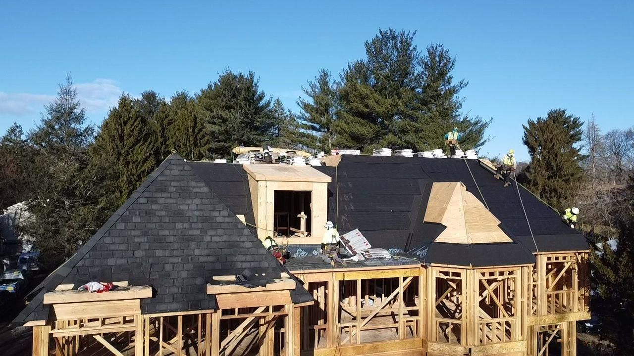 House under construction with a partially completed roof, surrounded by trees against a blue sky.
