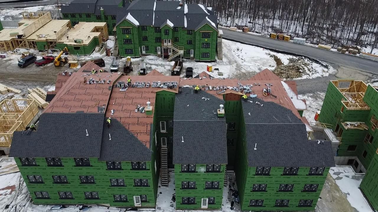 Construction site with multi-story buildings under development. Rooftops, green siding, and surrounding snow.