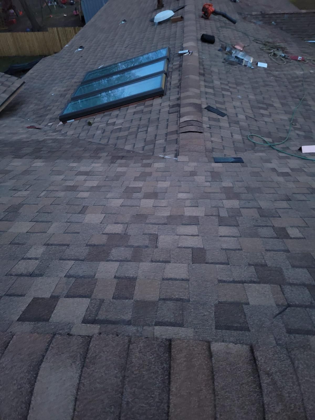 View of a roof with shingles, skylight, tools, and debris. Overcast.