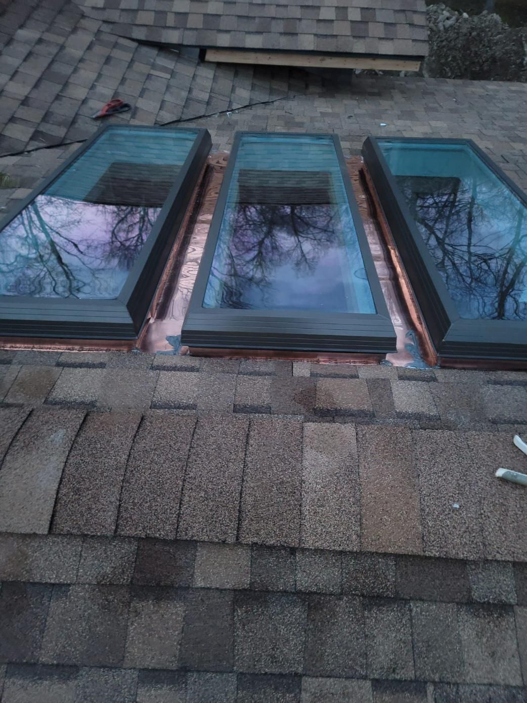 Three rectangular skylights installed on a shingled roof. Copper flashing visible around the skylights.