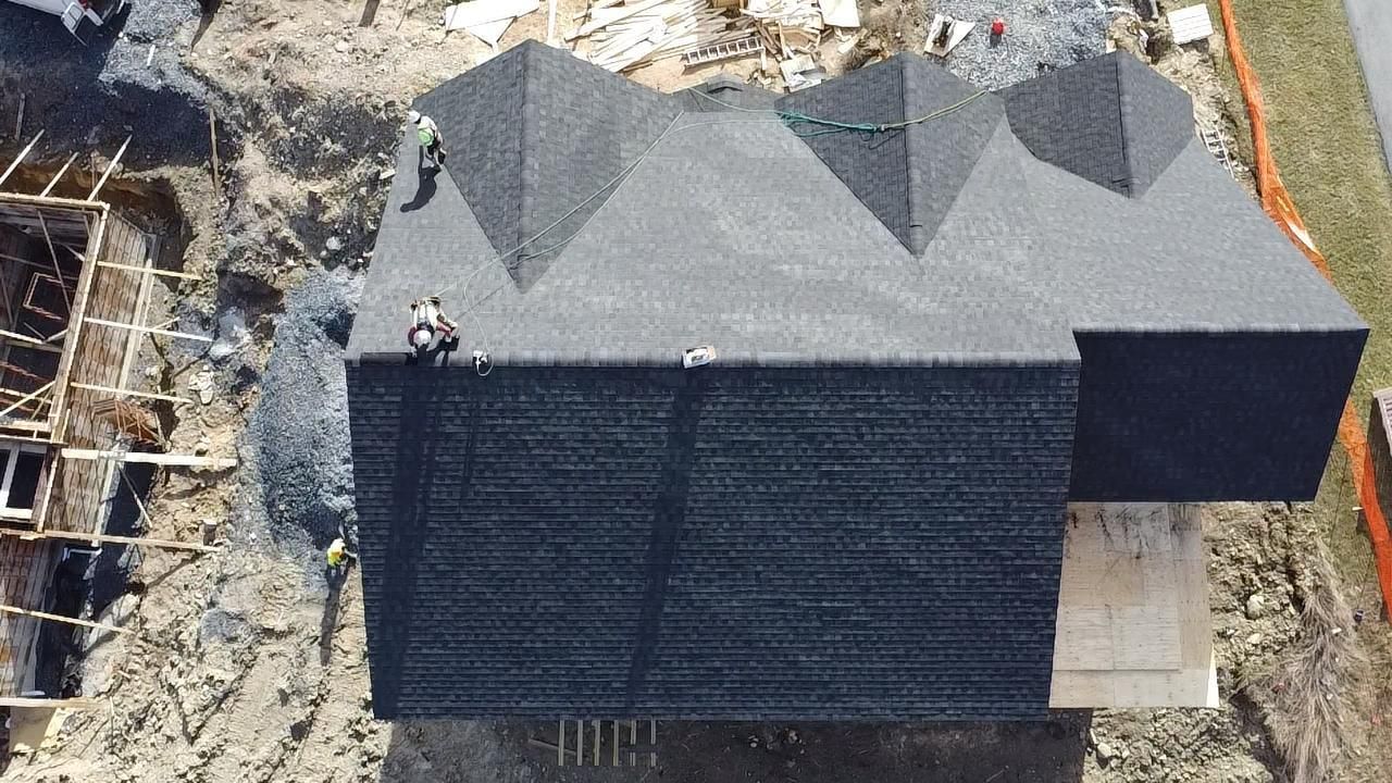 Overhead view of house under construction with workers on the roof, surrounded by building materials and dirt.