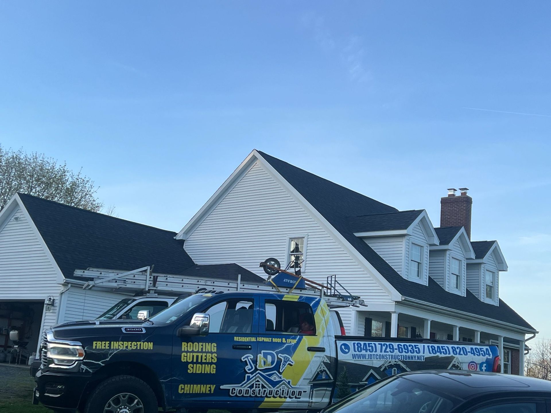 A white house with a black roof, a work truck is in front. The truck has company info on the side.