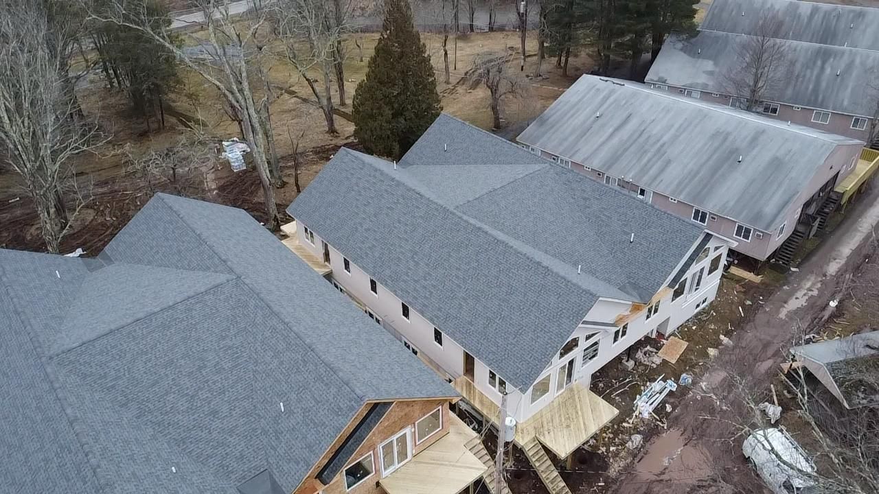 Aerial view of buildings with gray roofs and a forest backdrop.