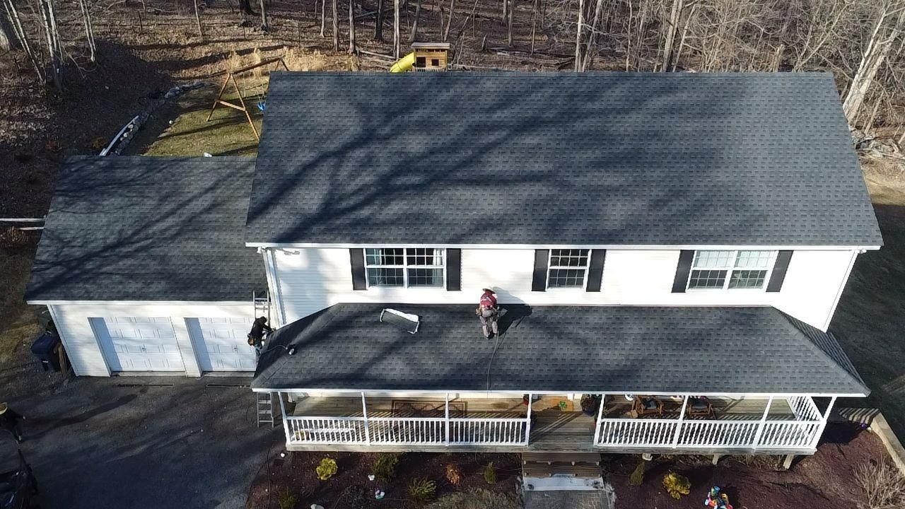 House with a new dark roof, a person on the roof, white exterior, and a porch.