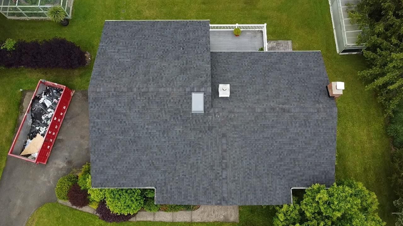Overhead view of a dark grey shingled roof, a white roof section, and a red dumpster beside the house.