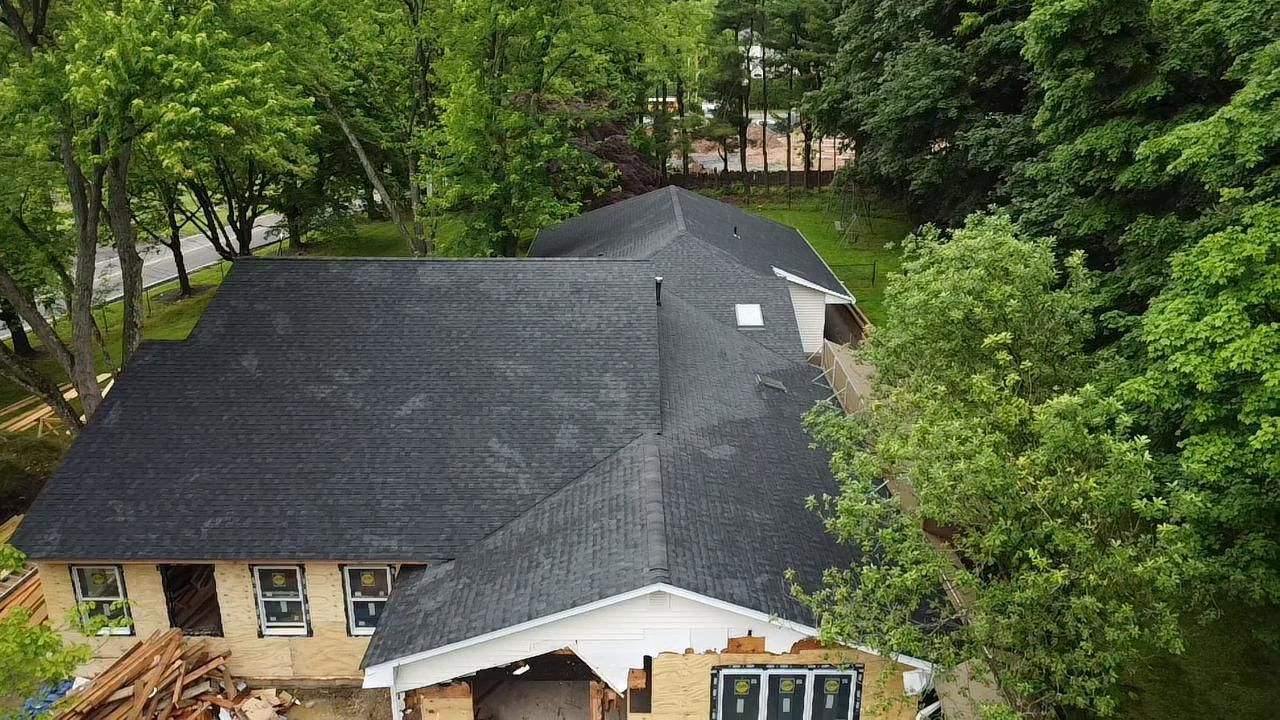 Aerial view of a house with a black roof surrounded by trees and a yellow brick facade.