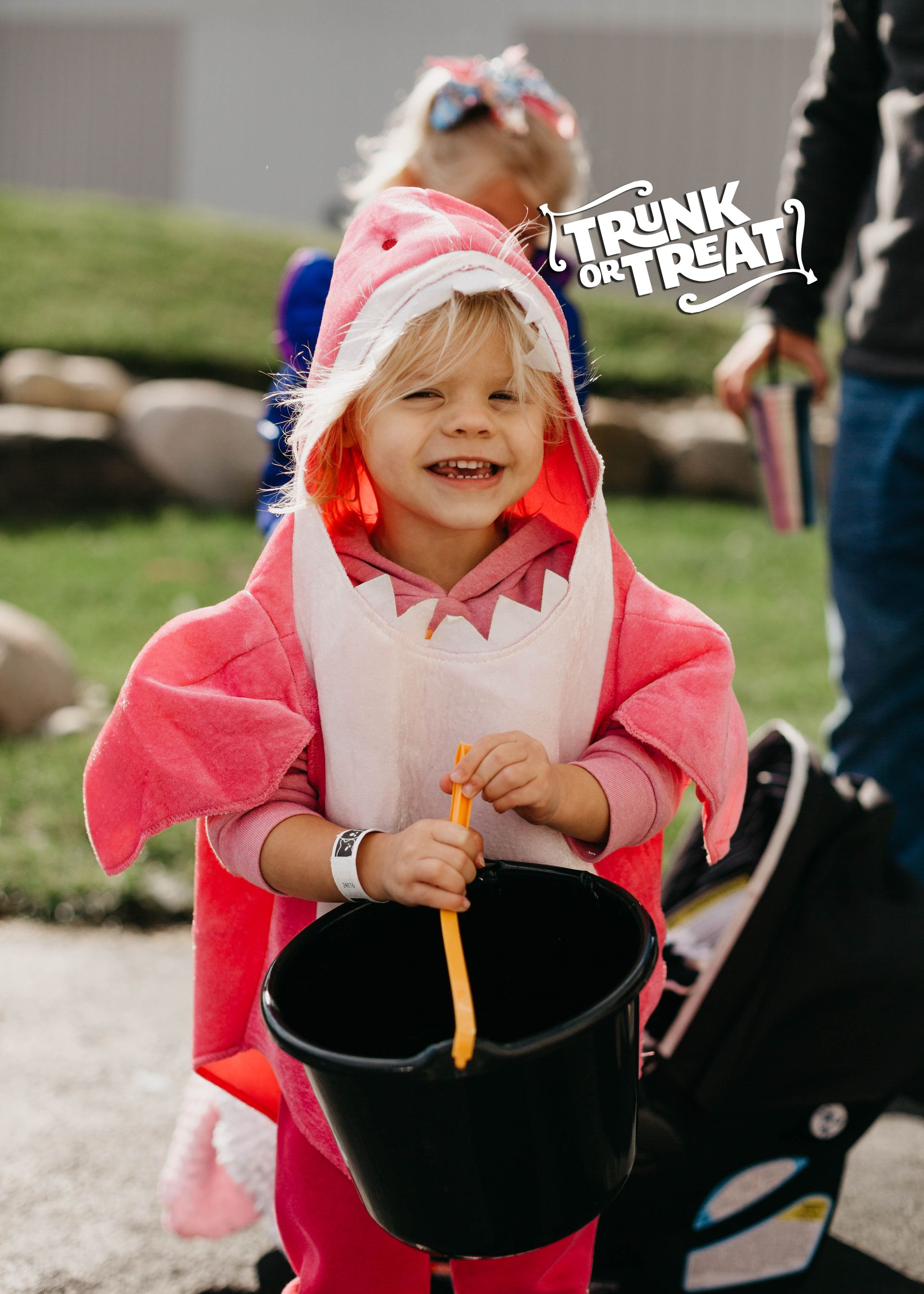 Child in pink costume holding a black bucket at a trunk-or-treat event
