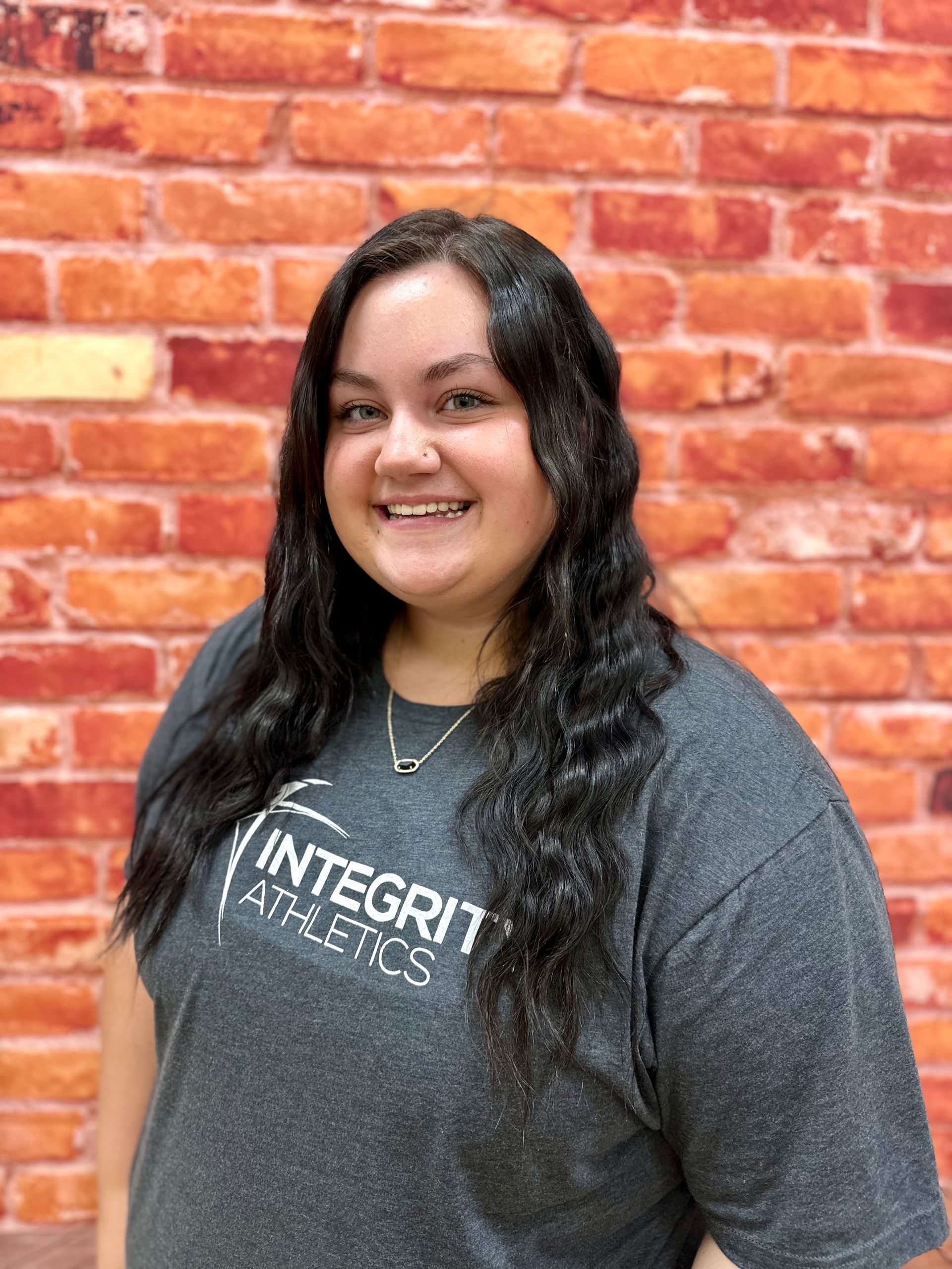 Smiling person in a dark gray Integrity Auto Sales T-shirt against a red brick wall