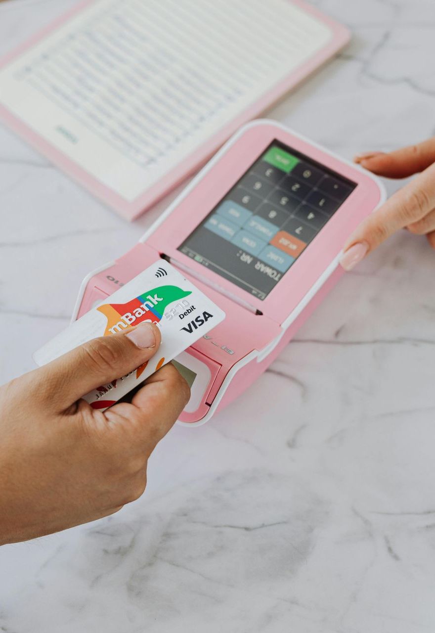 Hand inserting a card into a pink portable card reader on a marble desk