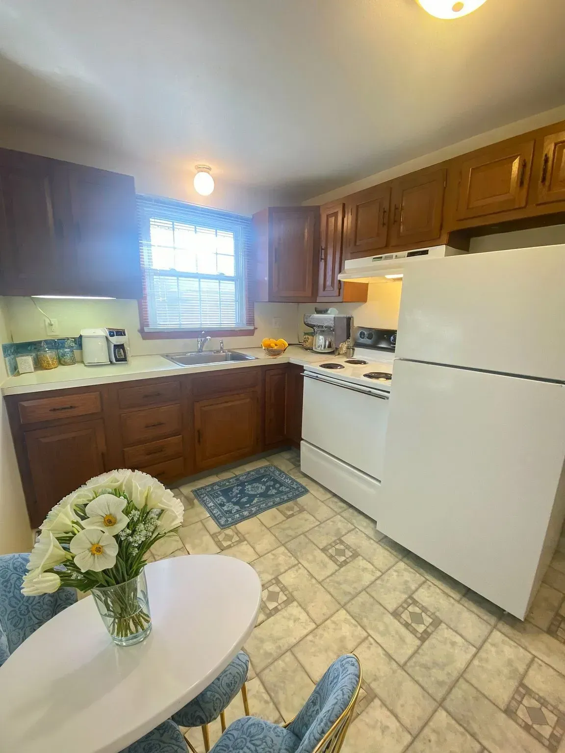 Small kitchen with dark wood cabinets, white appliances, tiled floor, and a round table with flowers.