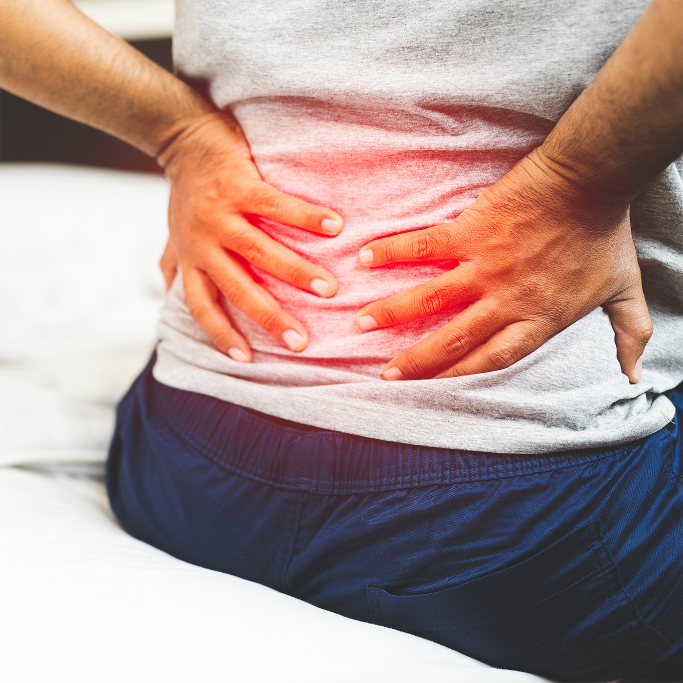 Person holding lower back with red pain highlight while sitting on a bed