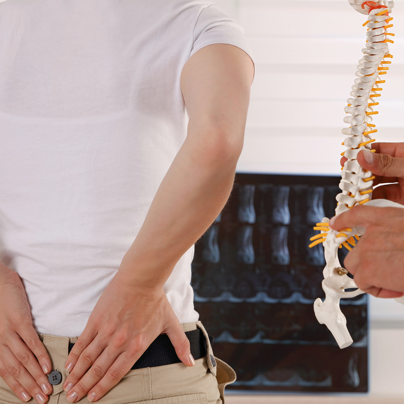 Person holding lower back beside chiropractor examining a spine model