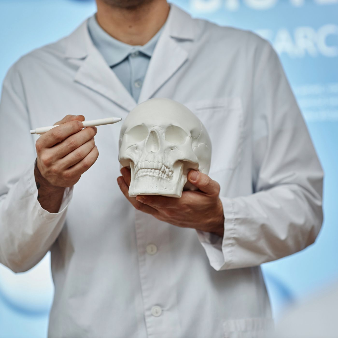 Lab technician in a white coat holding a human skull model and pointing with a pen
