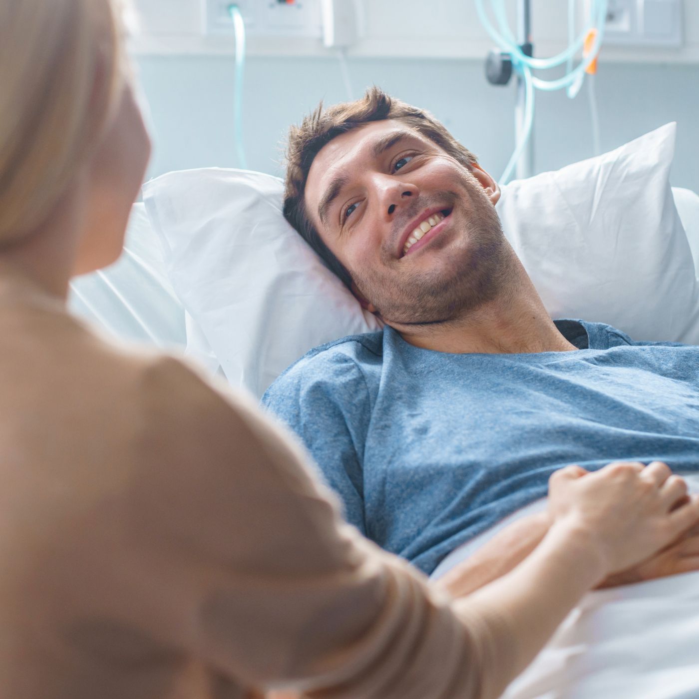 Smiling patient in a hospital bed holding hands with a visitor in a bright room