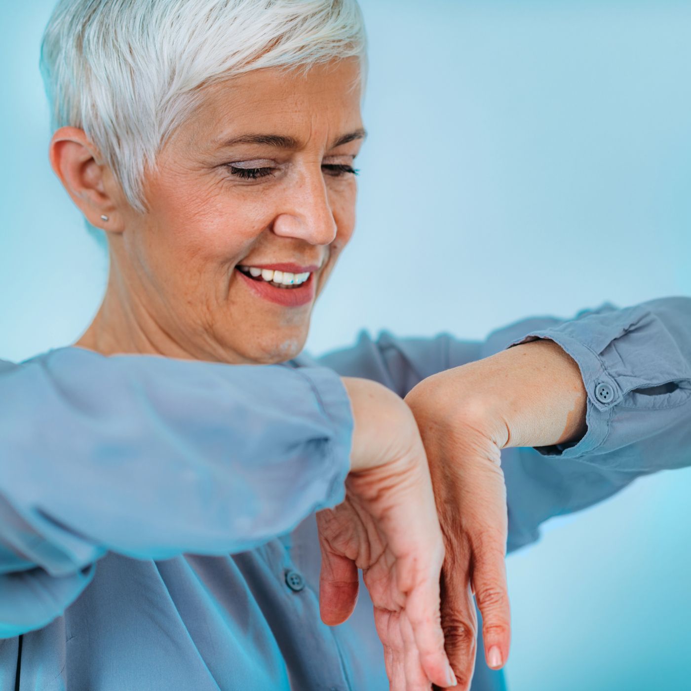 Smiling person with short white hair stretching arms against a blue background
