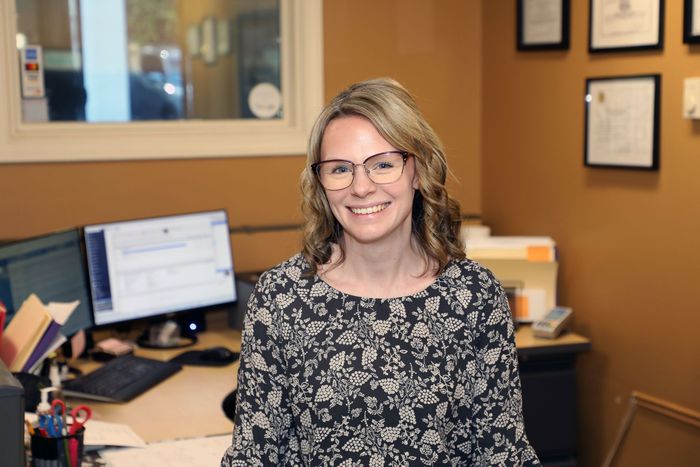 A woman wearing glasses is standing in front of a desk in an office.
