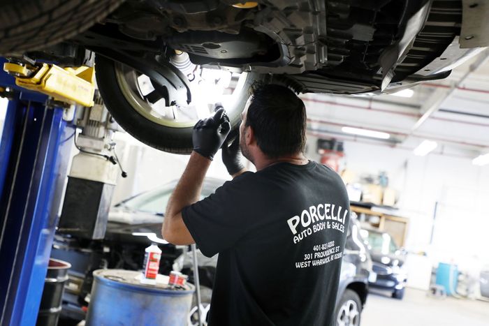 A man wearing a black shirt that says porcella is working under a car