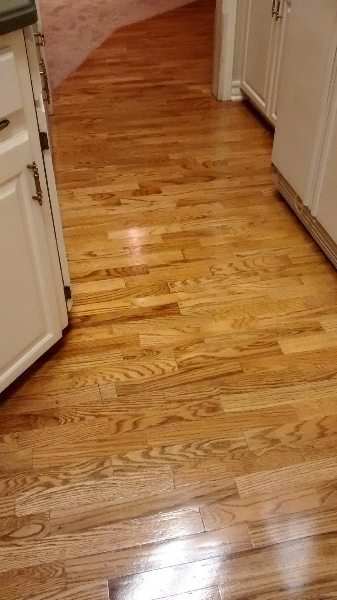 Shiny hardwood hallway floor with white cabinets on both sides and a doorway at the end