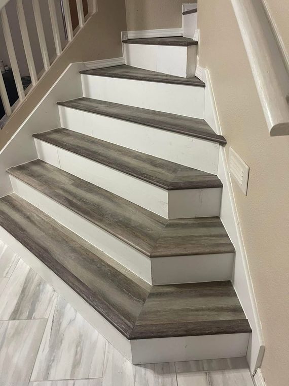 Indoor carpeted staircase with white railings and gray steps, viewed from the bottom.
