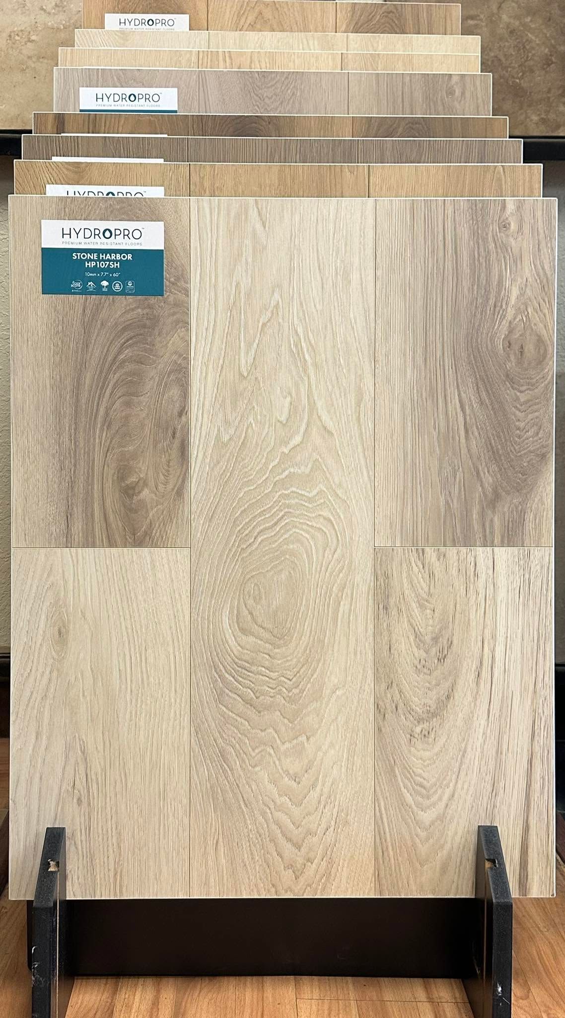 Stacked wood-look flooring samples in a store display, with beige and tan planks and labels on the top pieces