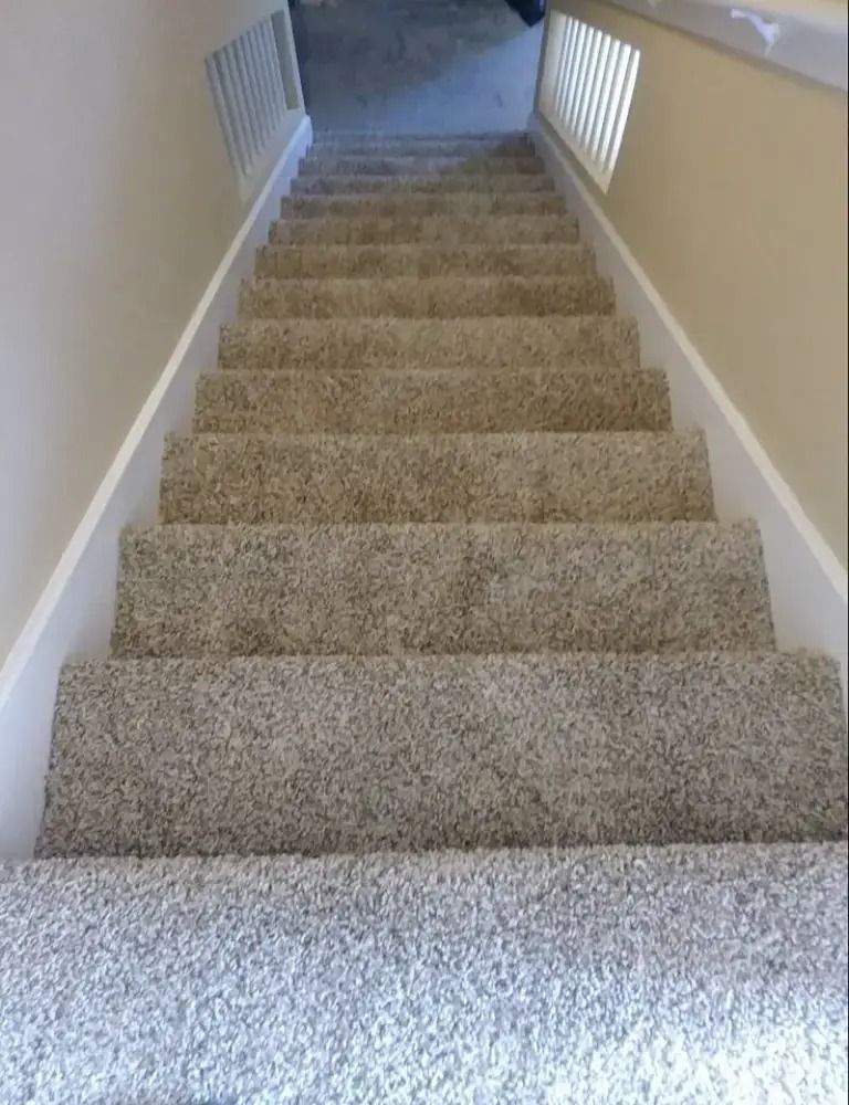 Carpeted indoor staircase with white railings and beige walls, viewed from the bottom looking up