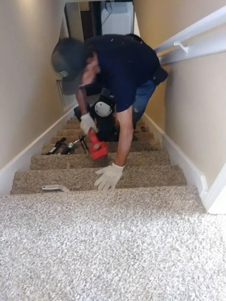 Worker vacuuming carpeted stairs with a red tool in a hallway.