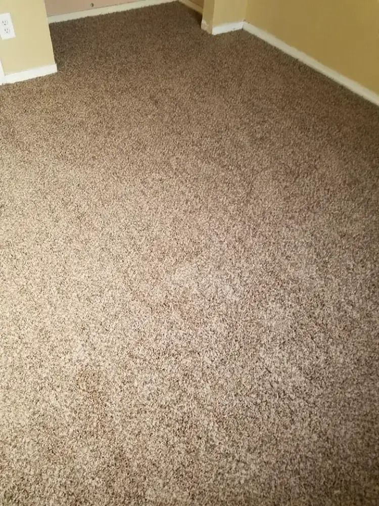 Empty beige carpeted room corner with tan walls and white baseboards.