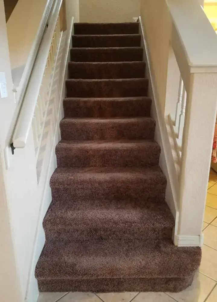 Carpeted staircase with brown runner between white walls and banisters