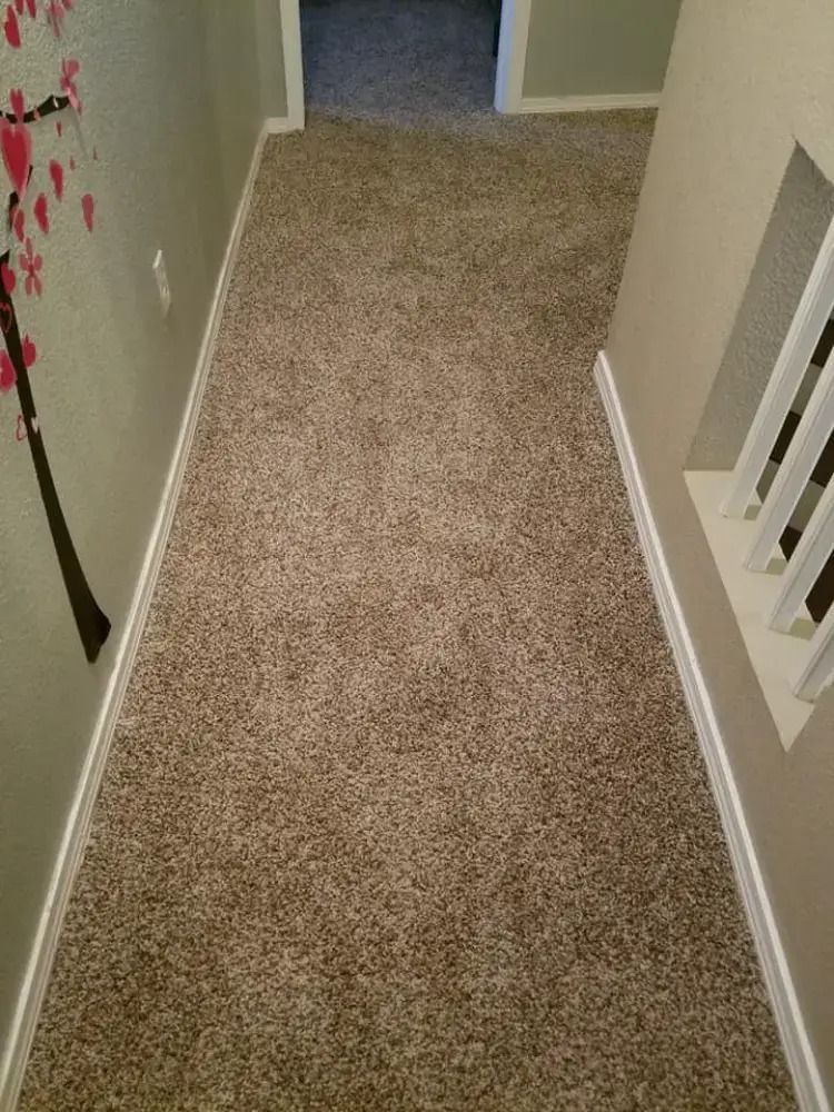Narrow carpeted hallway with beige walls and a doorway at the end.