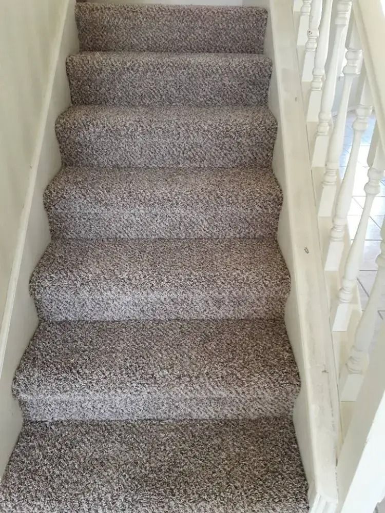 Carpeted staircase with white banister and beige walls, viewed from the bottom up