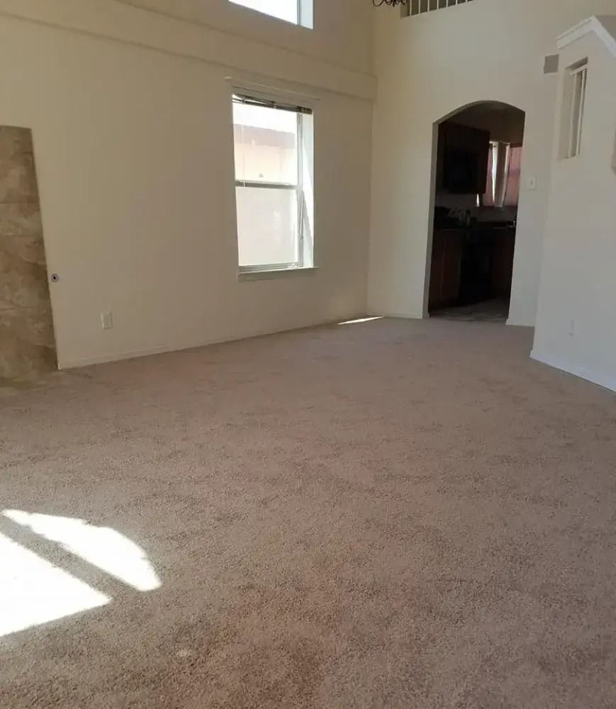 Empty beige carpeted living room with tall windows and an arched doorway